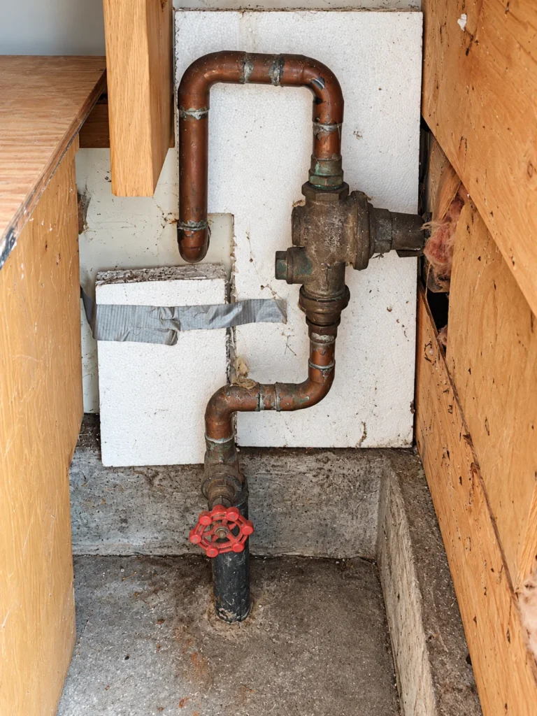 Old red-wheel gate valve beneath a PRV on copper pipe, illustrating a leaking main water shutoff valve