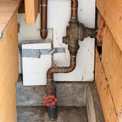 Old red-wheel gate valve beneath a PRV on copper pipe, illustrating a leaking main water shutoff valve